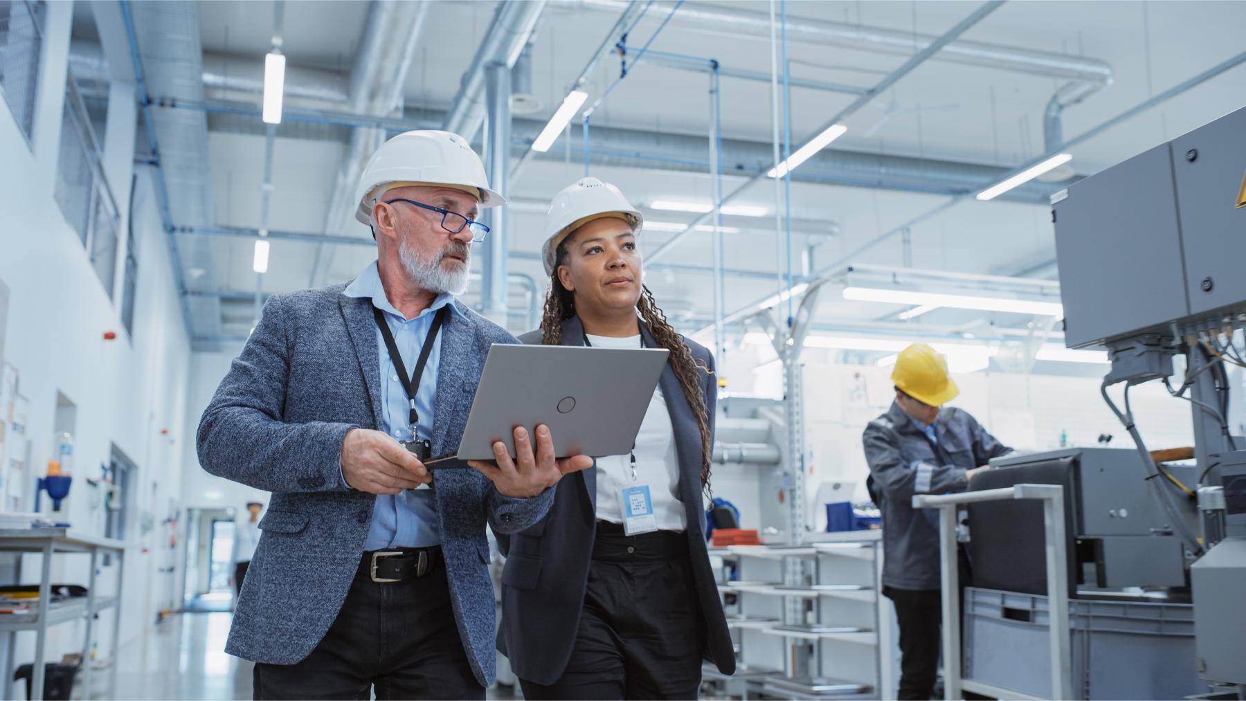 Two professionals in hard hats discussing over a laptop in a manufacturing facility, emphasizing teamwork and ethical practices relevant to DWI disclosure in CSP applications.